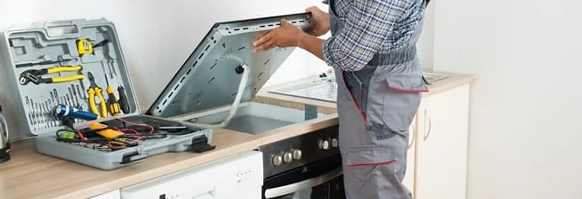 Cooktop repair technician lifting a built-in stovetop for service in Riverside, CA
