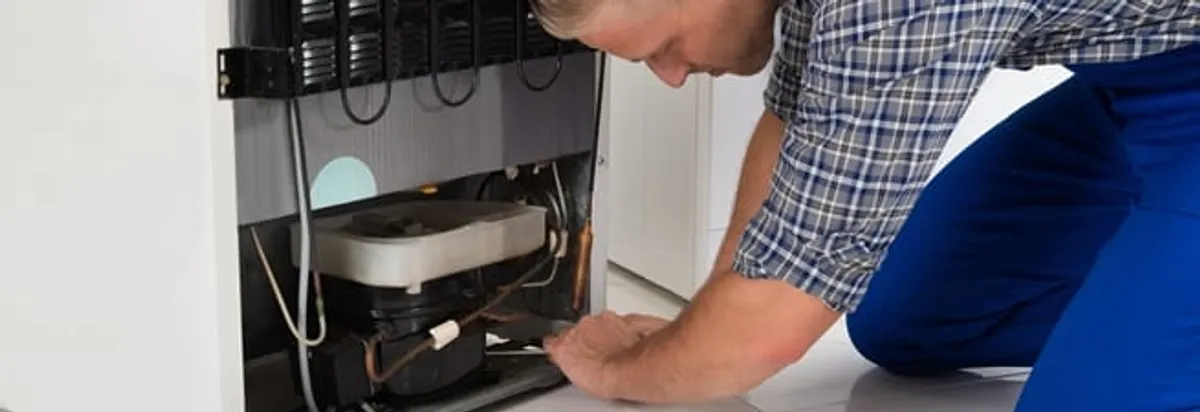 Refrigerator repair technician servicing the compressor and condenser area in Riverside, CA